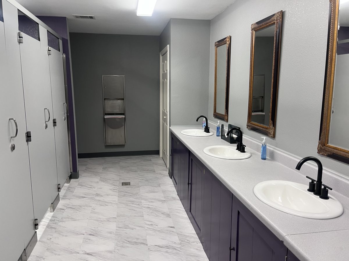 Finished commercial restroom viewed from the opposite end, with gray walls and a navy vanity